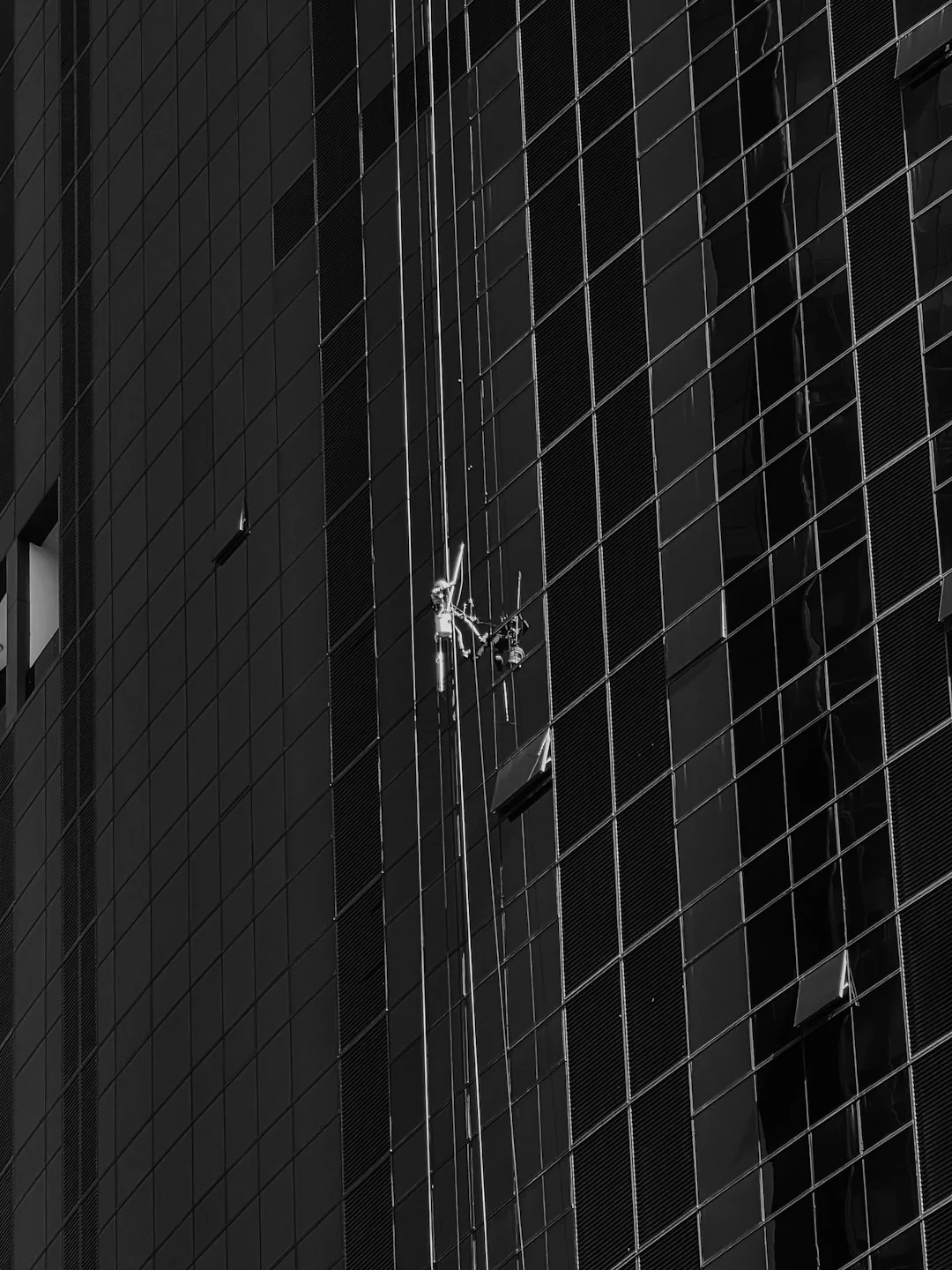 project-01-b Two workers are washing windows on a contemporary glass building front from a suspended platform.