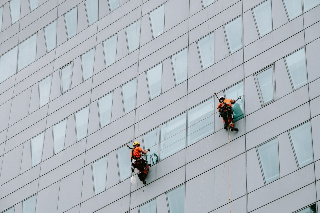 services-01 High-rise window washers in safety gear cleaning a skyscraper facade.